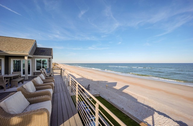 Impresionante casa frente a la playa con cubierta grande y anillo de fuego de gas a nivel del suelo.