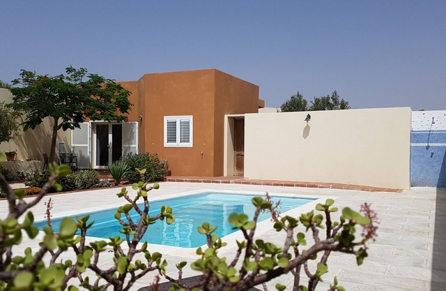 Casa con piscina entre jardines y finca de olivos.